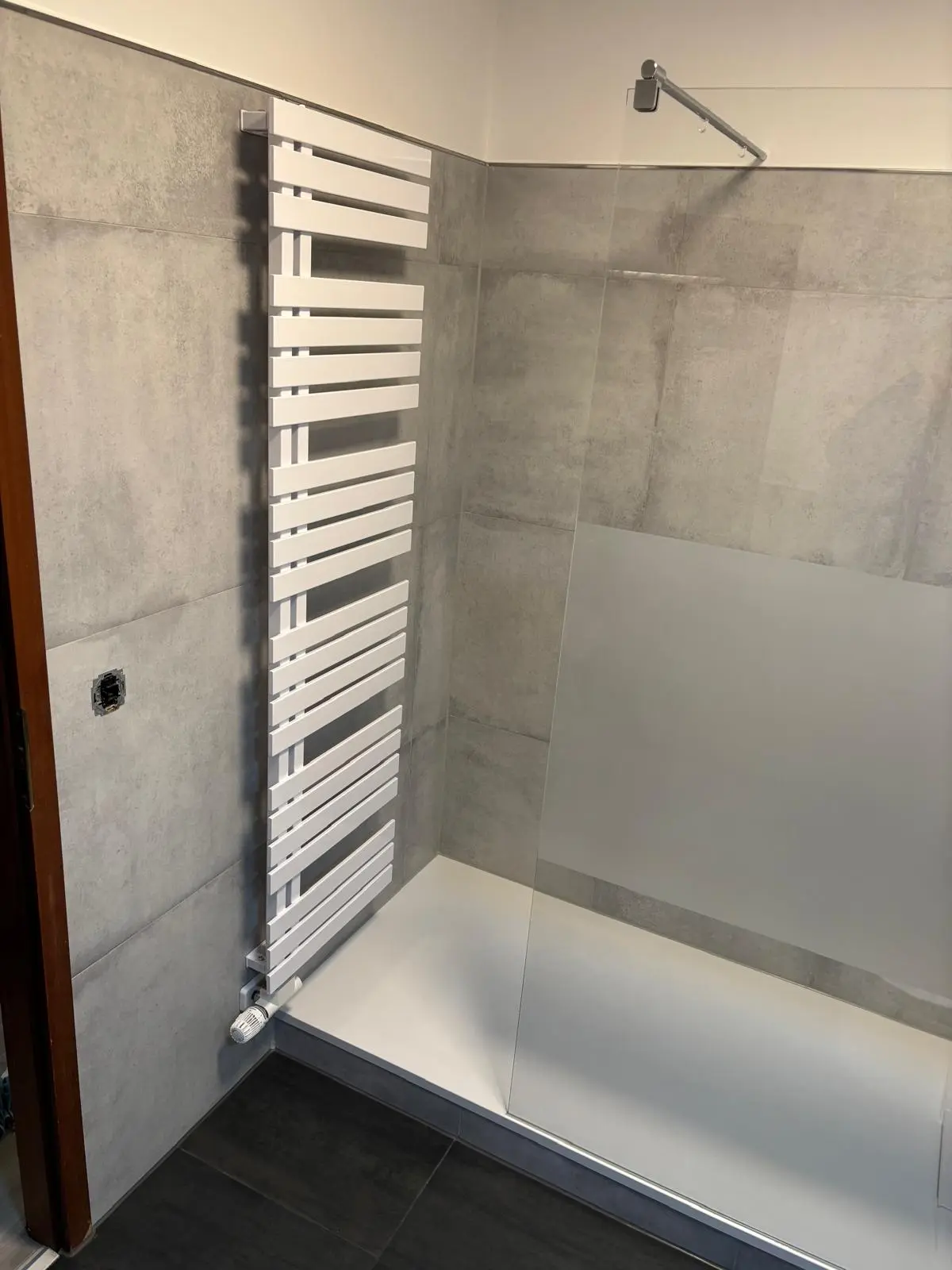 Badezimmer in Betonoptik: Graue Großformatfliesen in Kombination mit weißer Keramik und Glas - Joma Bau